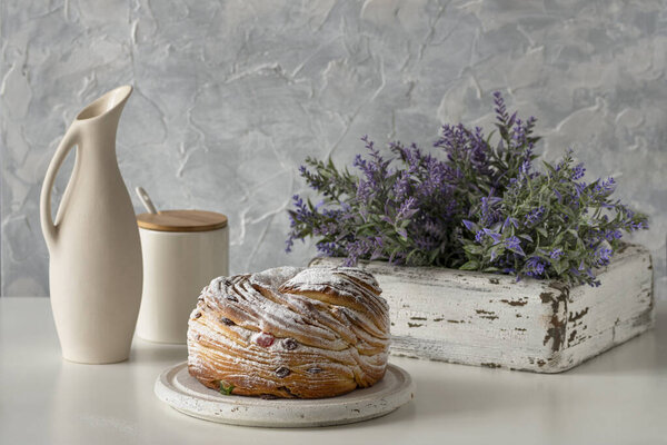 Easter still life of krafin standing on a white wooden tray, next to it is a jug andpurple  flowers in a white wooden box.  