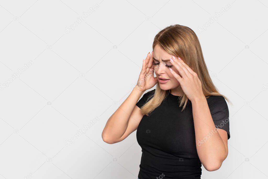 Studio shot of  young  woman in a black shirt clasping her head with her hands because of a headache from stress, isolated