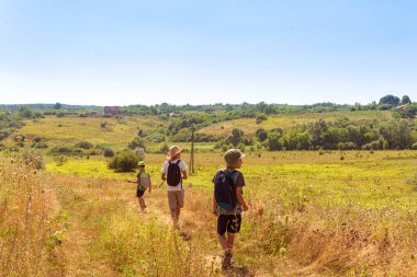 Shot of three young boys with backpacks  going hiking along the  field. Childhood concept