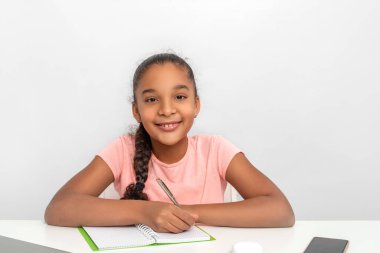 The schoolgirl sits at the table  indoors and does her homework 