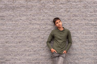 Half length portrait of a young dreaming guy wearing a green t-shirt standing against a textured grey brick wall 
