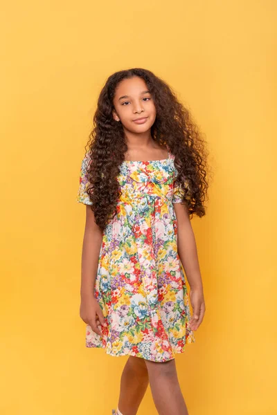 Half length portrait of a dark skinned young girl with long curly hair  on a yellow background