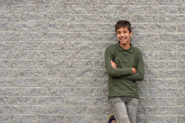 Waist up portrait of a young smiling guy wearing a green t-shirt standing with  arms crossed against a textured grey brick wall