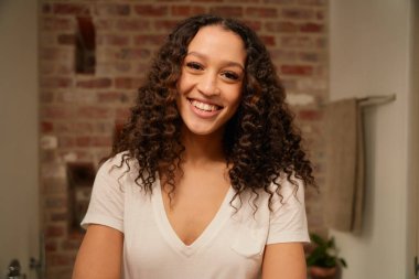 Çok kültürlü yetişkin bir kadın modern banyo aynasına mutlu bir şekilde bakıyor.