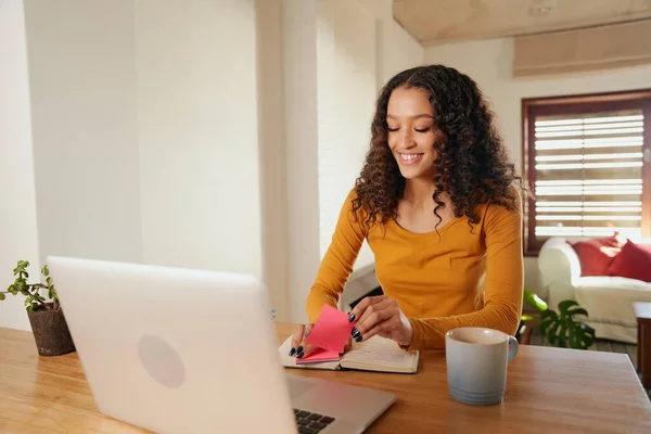 Mujer multicultural feliz, usando notas adhesivas en el cuaderno. Joven profesional trabajando a distancia con el ordenador portátil en apartamento moderno — Foto de Stock