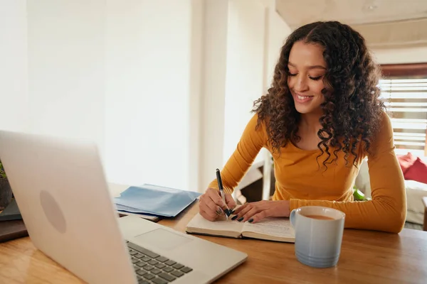 Multi-culturele vrouw werken vanuit huis, schrijven in notebook. Jong professioneel werken op afstand met laptop in modern appartement — Stockfoto