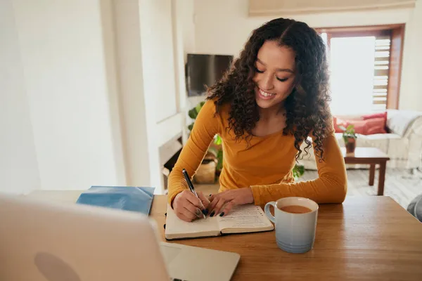 Multi-culturele vrouw gelukkig schrijven in notebook. Jong professioneel werken op afstand met laptop in modern appartement — Stockfoto