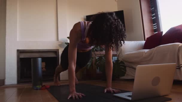 Jonge Afro-Amerikaanse vrouw oefenen yoga online in woonkamer stretching terug uit — Stockvideo