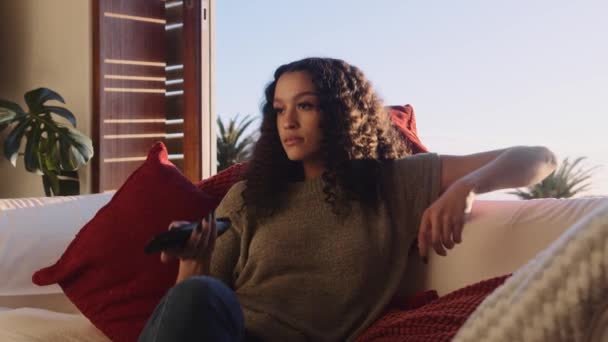 Genç, Afro-Amerikalı bir kadın evde oturup televizyon izleyip uzaktan kumandalı kanallar seçiyor. — Stok video