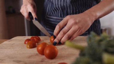 Mutfaktaki ahşap tahtada domates doğrayan çok kültürlü genç bir kadının ellerini kapatın. Taze ve sağlıklı