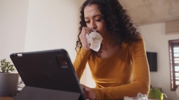 Malata multi-culturale giovane femmina soffiarsi il naso mentre si lavora su tablet elettronico in casa moderna. Telelavoro giovane professionista — Video Stock