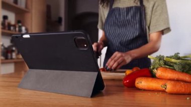 Afro-Amerikalı kadın mutfakta yemek pişiriyor. Dijital tablette tarifi takip eden aile için yemek yapıyor. 