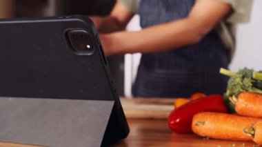 Tableti kapat. Modern mutfakta yemek pişirirken tabletten yemek tarifi okuyan çok kültürlü genç bir kadın. Taze meyve ve sebze.