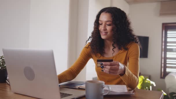 Zelfverzekerde multiculturele jonge volwassen vrouw die online aankopen doet met behulp van bankkaartgegevens, typt op laptop terwijl ze op afstand werkt vanuit een modern huis. — Stockvideo