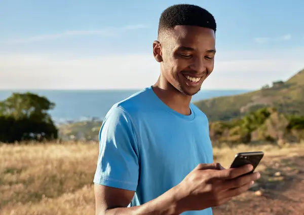 Black young Adult male smiling while using his cellphone, about to start mountain walk. Beautiful outdoors activity.