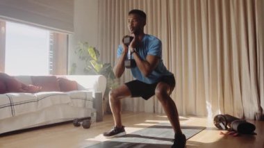 Genç Afrikalı Amerikalı erkek spor yapıyor ve salonda, bir spor paspasın üzerinde, dambıl ağırlığında, titreşimler atıyor. Evde çalışıp online ders alıyorum. 4K video