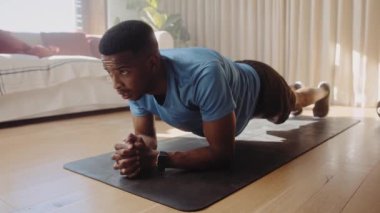 Genç Afro-Amerikalı zenci erkek, yoga minderinin üzerinde kalas pozisyonunda çalışıyor. Sağlıklı kalmak ve egzersiz yapmak Yüksek kalite 4K video