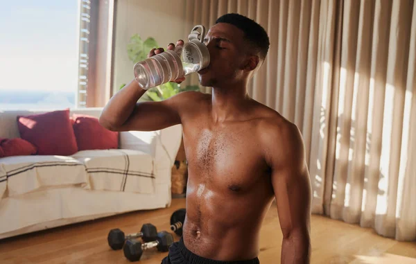 Genç kaslı zenci Afrikalı Amerikalı erkek egzersiz yaptıktan ve evde spor yaptıktan sonra su içiyor. Formda ve sağlıklı. Yüksek kalite fotoğraf