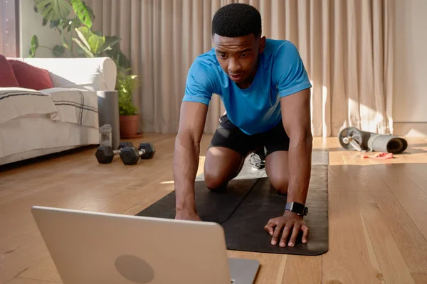 Genç Afro-Amerikalı erkek yoga minderinde egzersiz yapıyor dizüstü bilgisayar kullanarak online bir derse katılıyor, evde egzersiz yapıyor. Yüksek kalite fotoğraf