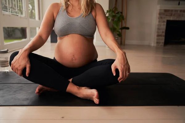 Beyaz hamile bir kadın, yoga minderinde dizlerini tutarken bacak bacak üstüne atarak oturuyor. Evde sağlıklı bir hayat sürüyor. Yüksek Kalite Fotoğraf