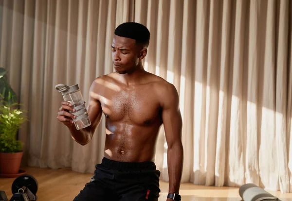 Young African American black male athlete drinking water after a high intensity exercise workout at home doing an online class. Keeping fit and healthy .High quality photo