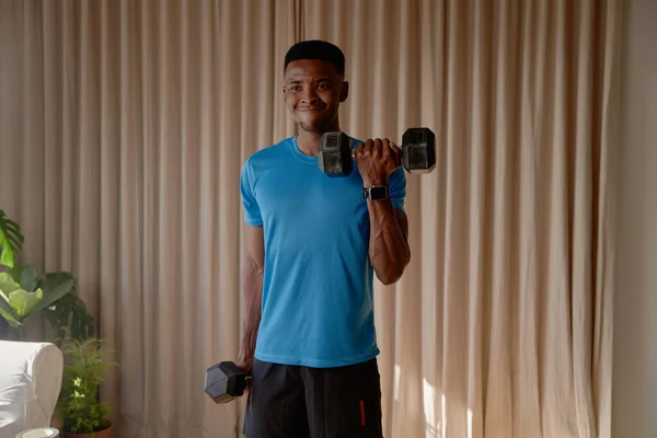 Young African American Black male doing bicep curls using dumbells and doing an intense weight training, working out at home gym High quality photo