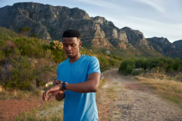 Black young Adult male checking the time on his smart watch. Sportsman training in the mountains for his trail run. High quality photo