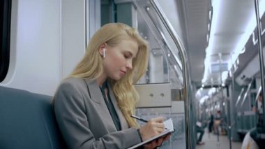 Metroda oturan, günlük yazan, kulaklık takan iş sarışını kız.