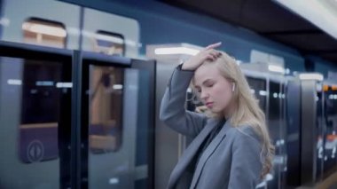 Uzun saçlı iş sarışını metro bekleyen kız, arkasında tren var.