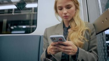 Genç sarışın iş kızı modern metroda oturuyor ve telefonuna bakıyor.