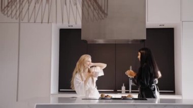 Genç esmer ve genç bir sarışın mutfakta pijamalarıyla dans ediyorlar.