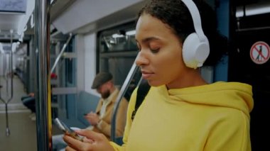 Metroda duran, kulaklık takan ve telefonuna bakan genç bir kız.