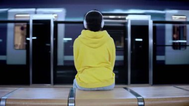 Kulaklık takan genç bir kadın metro treninin istasyona varmasını bekliyor.