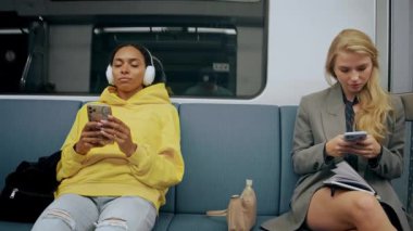 İşten sonra modern metro treninde oturan iki genç kız telefonlara bakıyor.