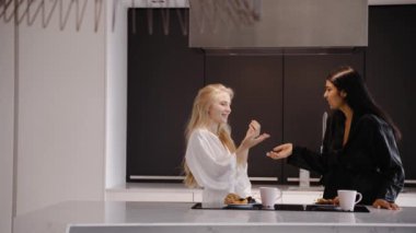 Genç esmer ve genç bir sarışın mutfakta pijamalarıyla gülümsüyor.