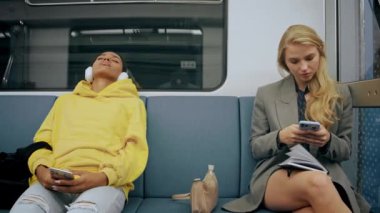 İşten sonra modern metro treninde oturan iki genç kız telefonlara bakıyor.