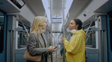 Modern metro treninde iki kız sohbet ediyor ve gülümsüyor. Tırabzanlara tutunuyorlar.