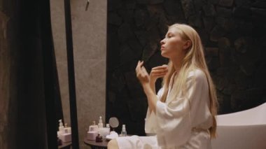 Banyoda genç bir sarışın aynanın önünde oturuyor boynunu ve yüzünü siliyor.