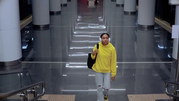 Jeune fille monter les escaliers dans la gare moderne, portant des écouteurs — Video