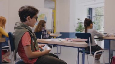 Çocuk ders sırasında masanın altında gezici oyunlar oynuyor ve yakalanıyor.