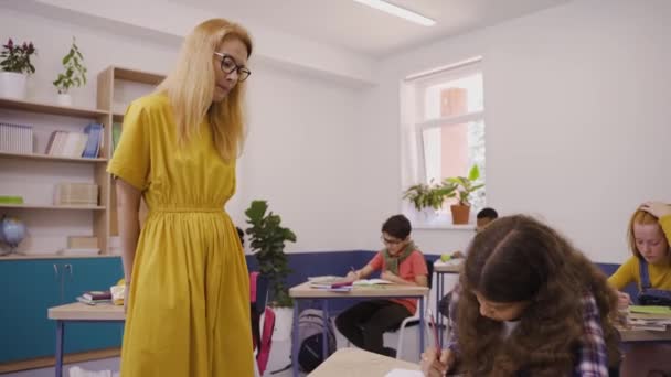 Nauczycielka pomaga ciężko pracującym uczniom napisać test w szkole podstawowej. — Wideo stockowe