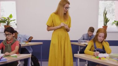 Bayan öğretmen, ilkokulda öğrencilerin bir sınav yazmalarına yardım ediyor.