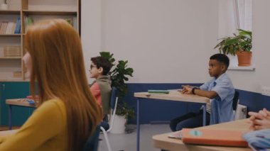 Çocuk soru sormak için elini kaldırıyor, çocuklar dikkatle dinliyor hoca.