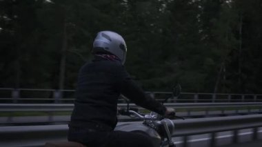 Otoyolda gün batımında ormanda motosiklet süren bir adam var.