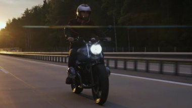Gün batımında, otoyolda motosiklet süren bir adam.
