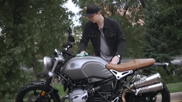 Νεαρός άνδρας σκούπισμα scrambler μοτοσικλέτα του με πανί στο δρόμο μετά το πλύσιμο — Αρχείο Βίντεο