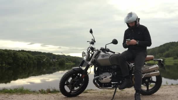 Kierowca motocykla wiadomości i patrząc na jego telefon siedzi na zachodzie słońca — Wideo stockowe