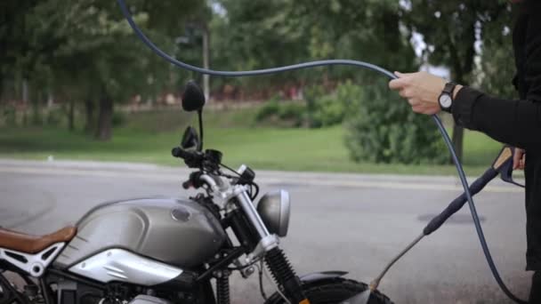 Jovem lavando sua moto scrambler com mangueira de água na rua — Vídeo de Stock