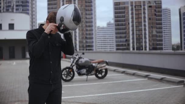 Le gars porte un casque de moto sur le parking, devant la moto — Video