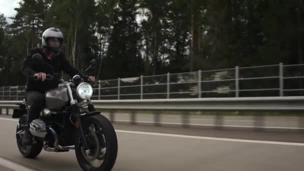 Άνθρωπος ιππασία scrambler μοτοσικλέτα στην εθνική οδό μέσα από το δάσος, πλαϊνή άποψη — Αρχείο Βίντεο